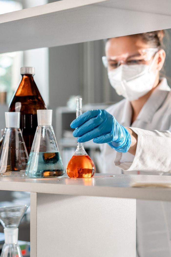 services-01 Scientist in protective gear handling chemical solutions in a laboratory setting.